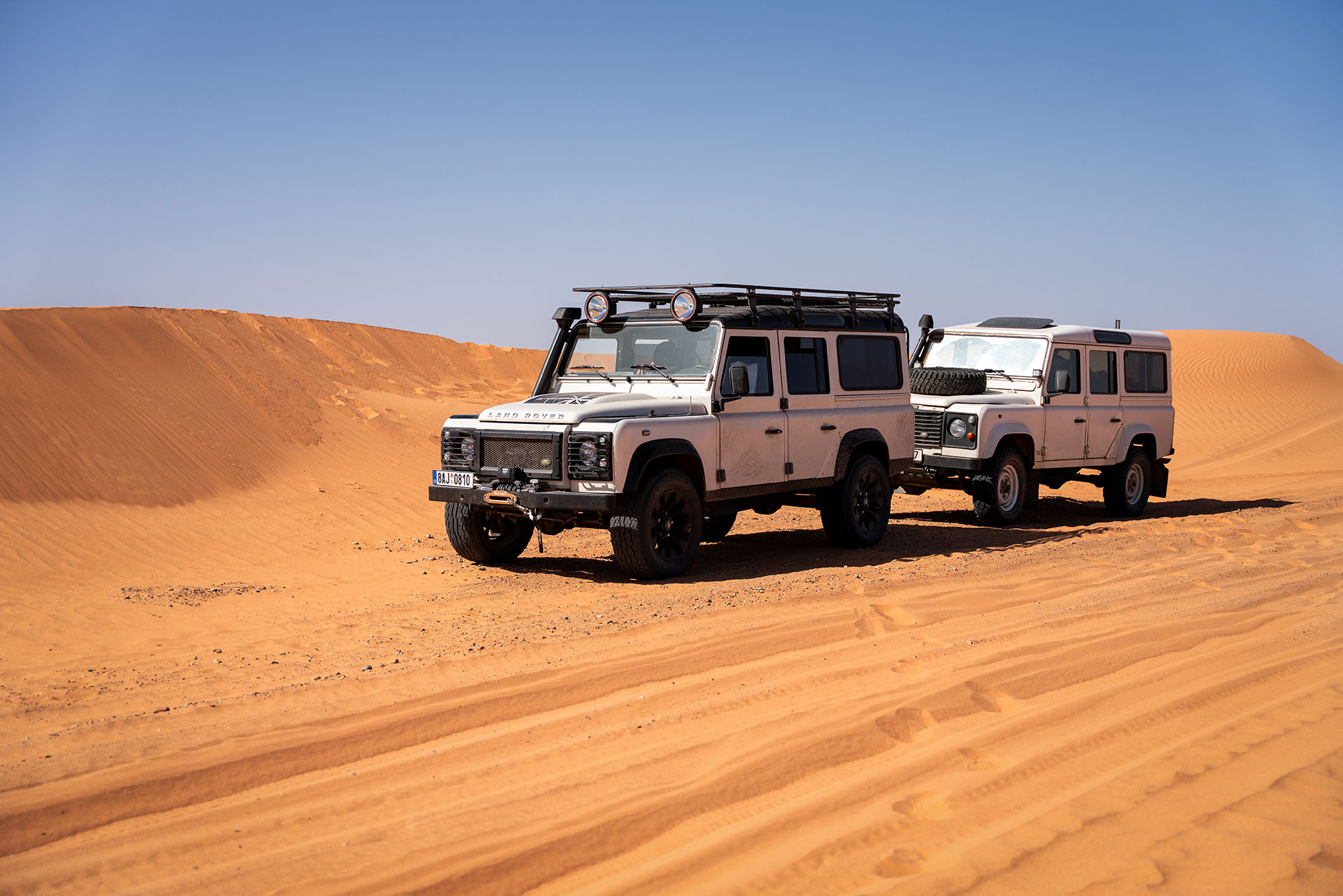 Dva vozy Land Rover Defender v písečných dunách během expedice v Maroku.