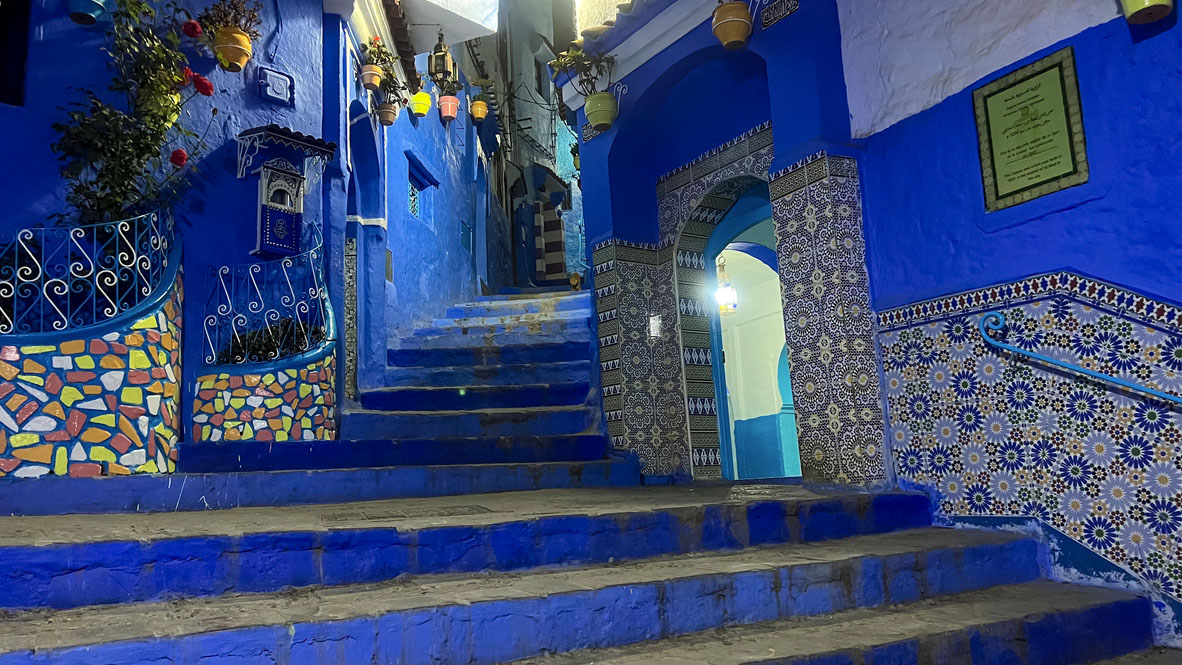 Modře vymalovaná historická ulička se schody a tradičními mozaikami ve městě Chefchaouen